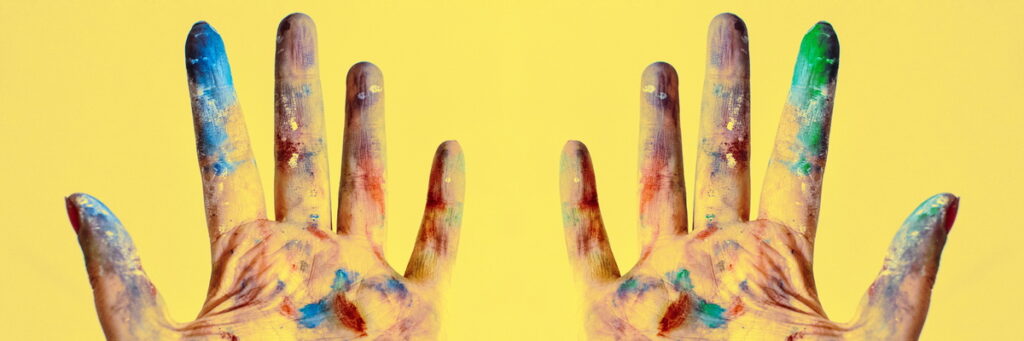 hands, palms up, stained with blue, green, purple, yellow, and white paint over a yellow background